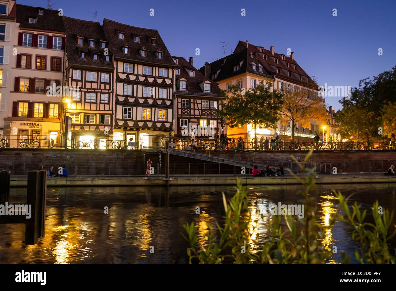 Ville nocturne de Strasbourg, traversée par la rivière. Les bâtiments sont vieux et les gens sont rassemblés sur la rive de la rivière. 10/15/2025 Banque D'Images