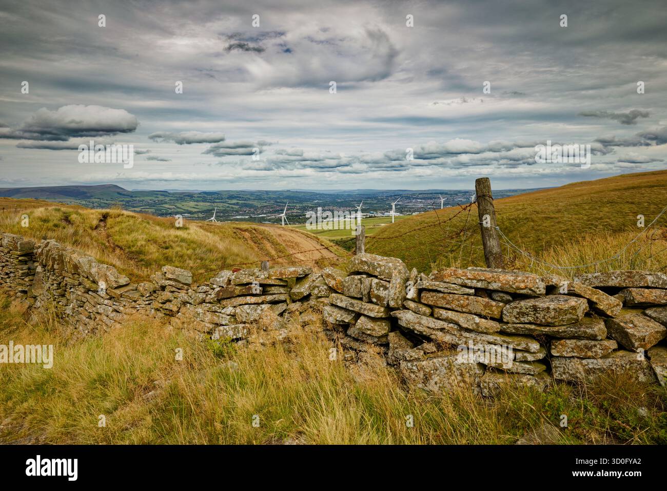 Un mur de pierres sèches et des poteaux de clôture dans un paysage montagneux regardant vers un parc éolien sur le bord d'une ville dans une vallée, Burnley, Lancashire. Banque D'Images