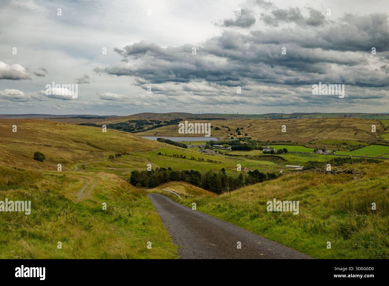 Une étroite route rurale serpente à travers un sombre paysage de landes Pennine avec un réservoir dans une vallée lointaine, Burnley, Lancashire. Banque D'Images