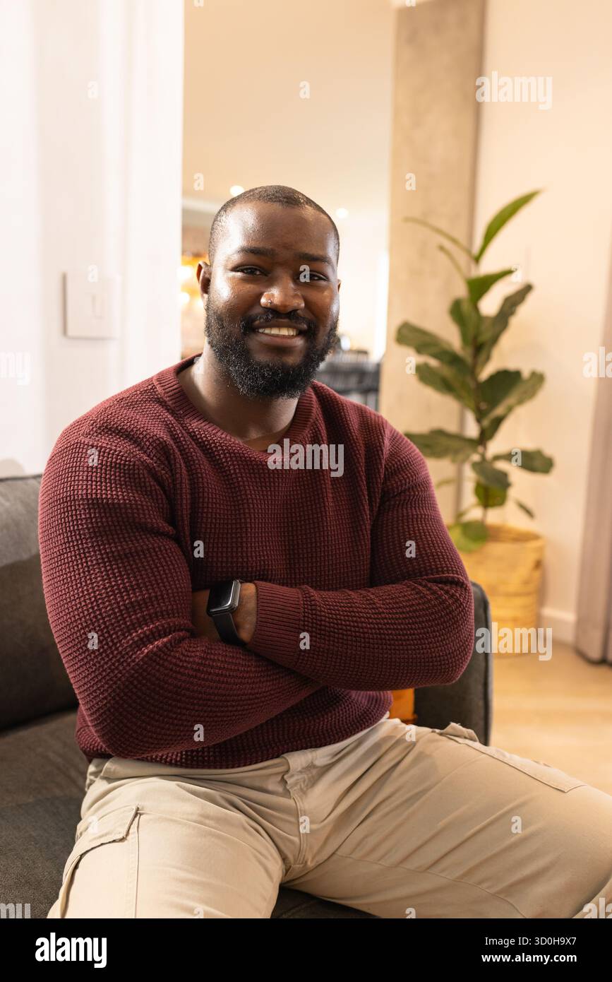 Homme afro-américain assis sur le canapé portant smartwatch et pull dans le salon Banque D'Images