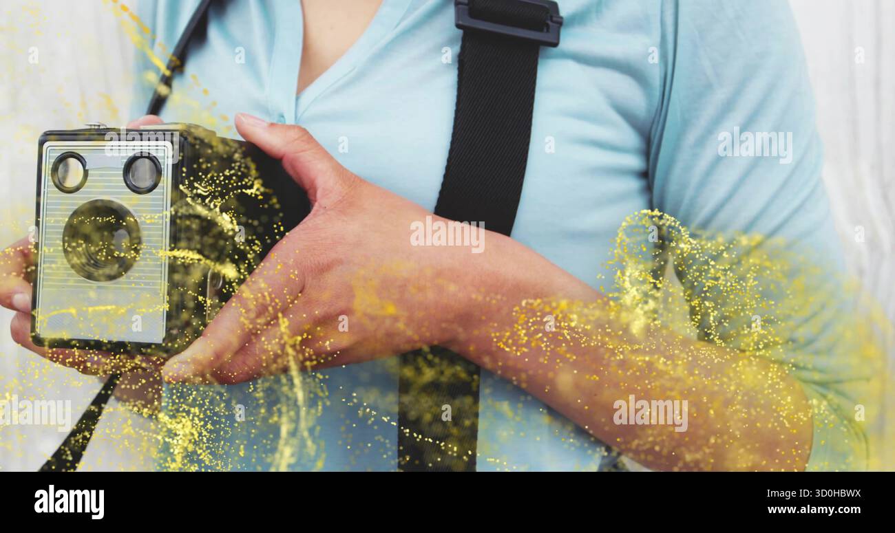 Tenant la femme portant le dessus bleu et la sangle noire montrant la caméra de boîte en studio, éclaboussures jaunes Banque D'Images