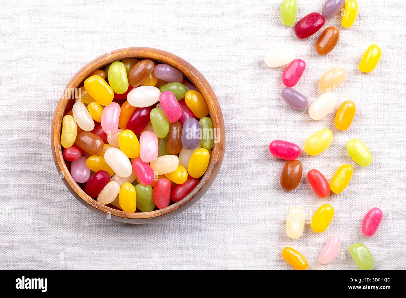 Gelée de haricots, assortiment de saveurs et de couleurs, dans un bol en bois, sur lin. Petits bonbons au sucre en forme de haricots avec des coquilles de bonbons souples et des intérieurs en gel épais. Banque D'Images