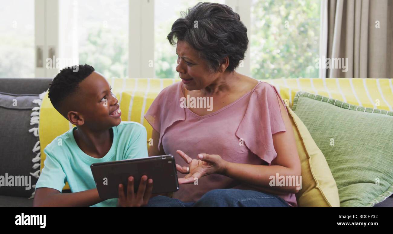 Guide grand-mère et petit-fils explorant la tablette à la maison, avec canapé jaune jeté coussin vert Banque D'Images