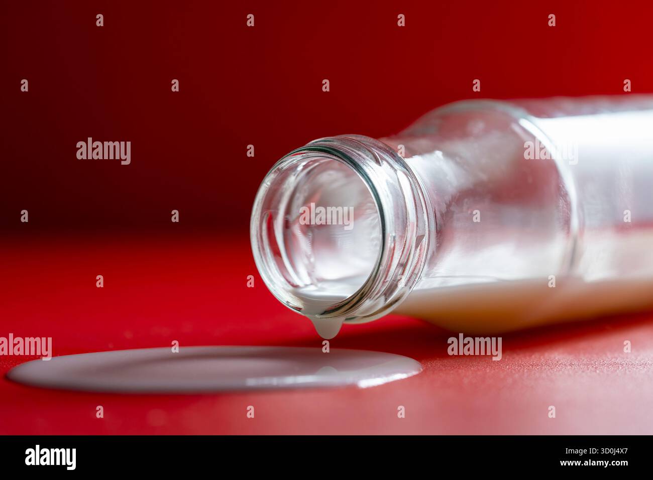 Bouteille en verre avec du lait renversé sur un fond rouge, gros plan Banque D'Images Bouteille en verre avec du lait renversé sur un fond rouge, gros plan Banque D'Images