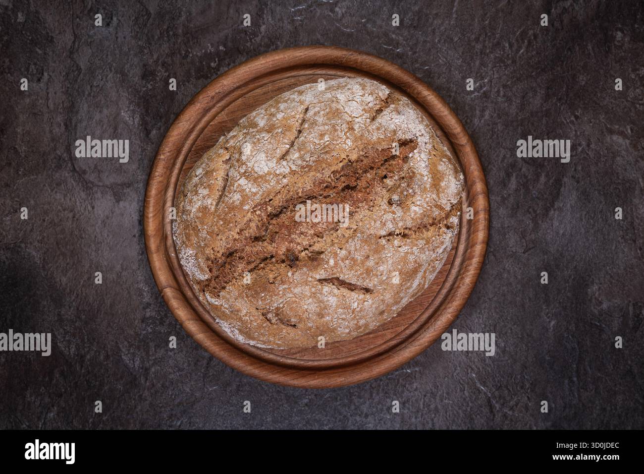 Pain complet d'épeautre rond de levain avec noix sur planche de bois ronde, vue de haut en bas montrant la croûte, composition centrée. Banque D'Images