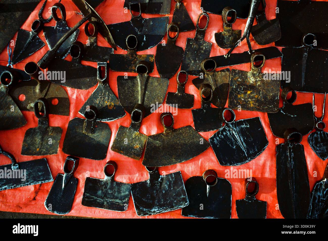 Pièces d'outils de creusement en métal assorties exposées sur un sol en nylon rouge sur un marché extérieur, capturées dans un style graphique analogique. Banque D'Images