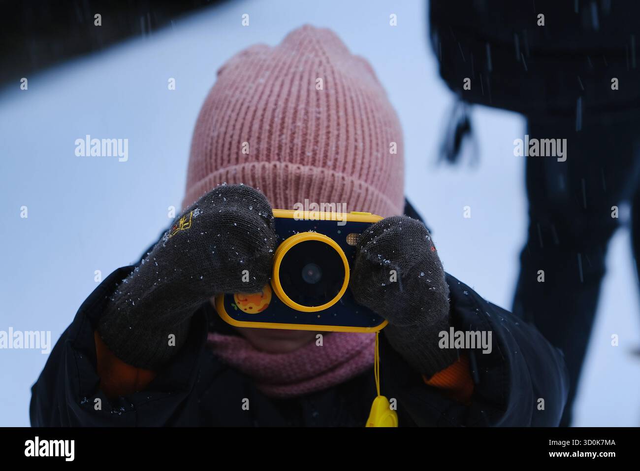 Enfant prenant des photos avec un appareil photo coloré dans la neige d'hiver portant des vêtements chauds et des moufles Banque D'Images