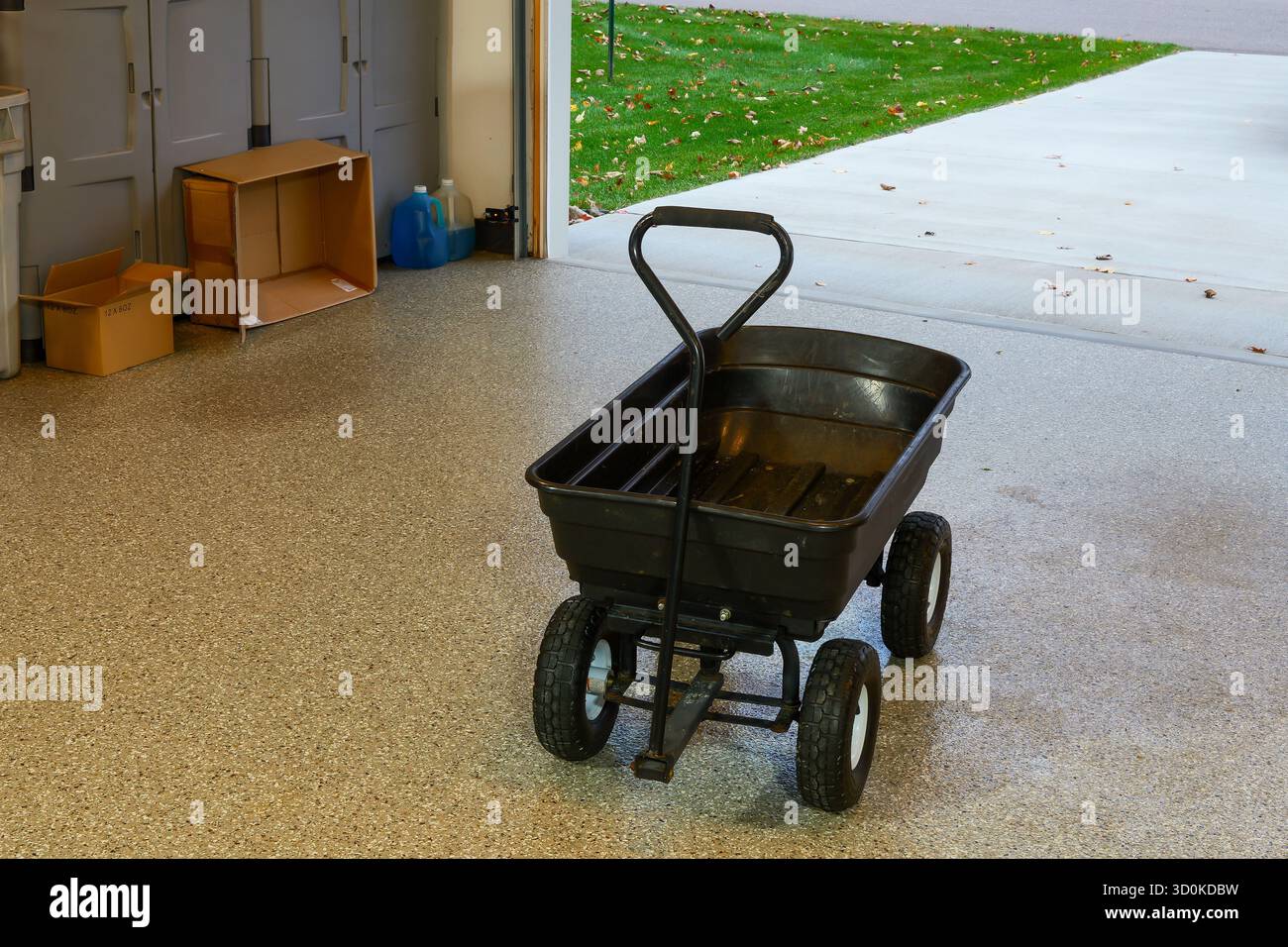 Un chariot de jardin noir sur le plancher recouvert d'époxy du garage. Banque D'Images