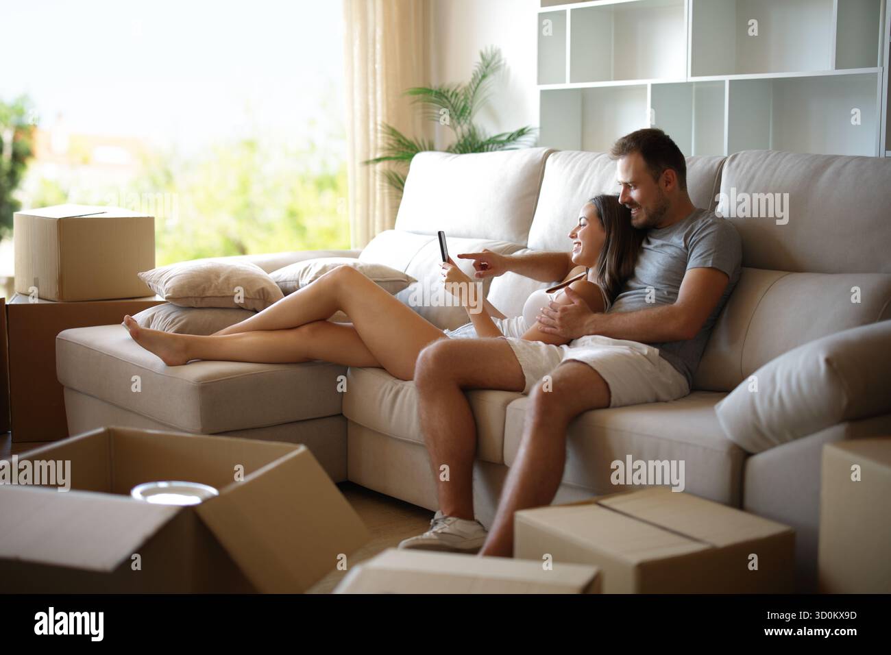 Heureux couple se reposant tout en déménageant à la maison vérifier le téléphone assis sur un canapé à la maison Banque D'Images