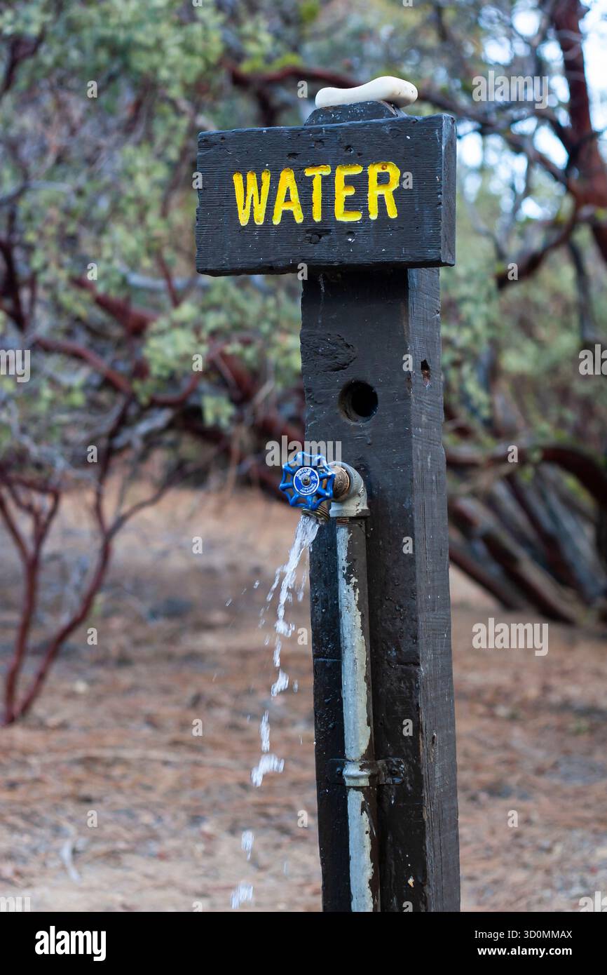 Robinet d'eau de camping rustique avec ruisseau coulant et panneau en bois Banque D'Images