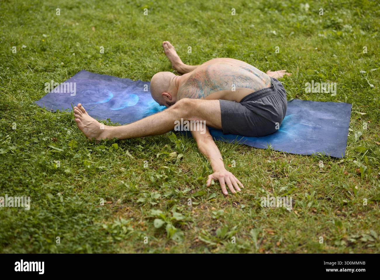 Homme flexible effectue la pose de yoga sur tapis dans le parc herbeux Banque D'Images