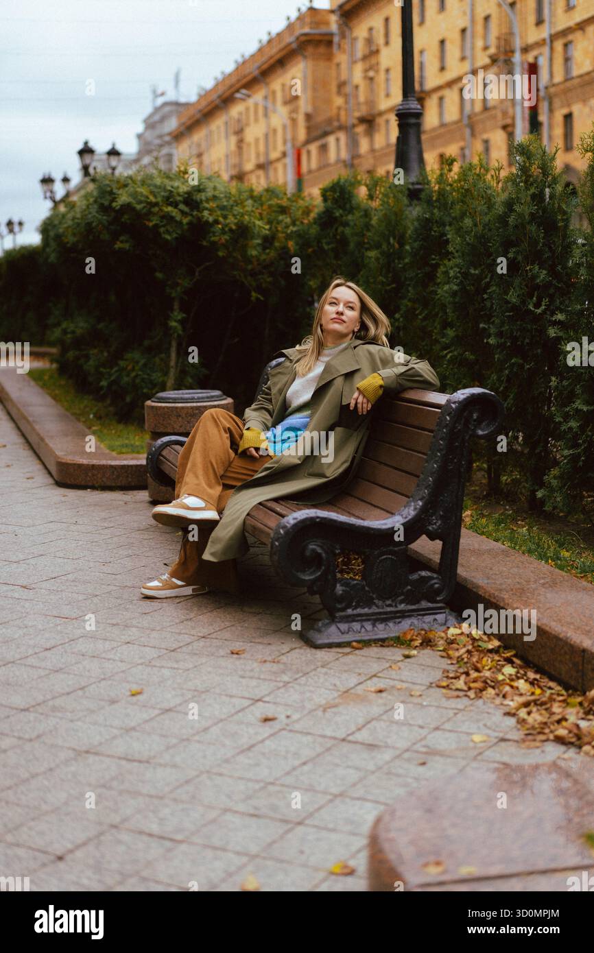Femme se relaxant sur un banc de parc en tenue d'automne décontractée avec des baskets Banque D'Images