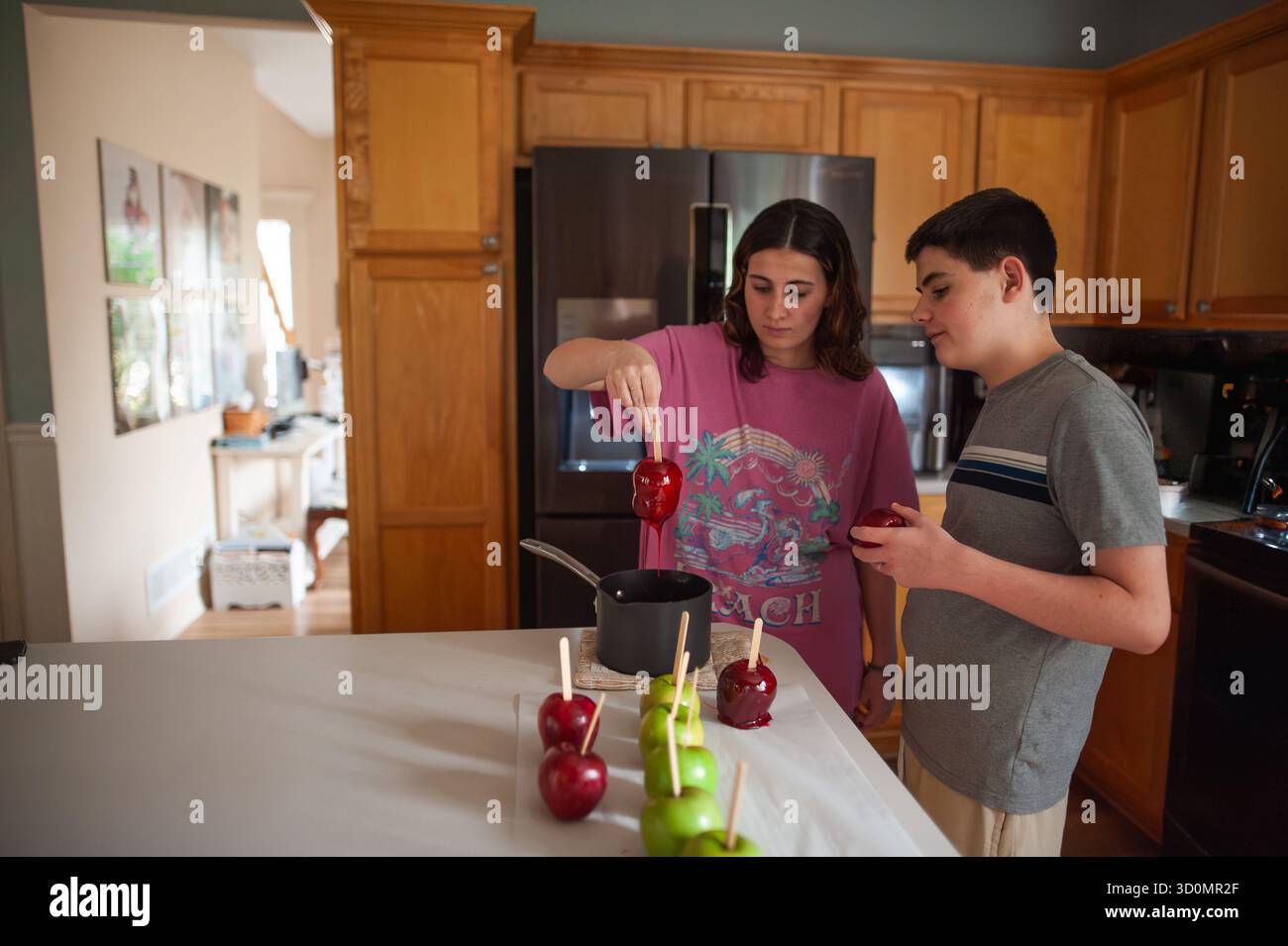 Frères et sœurs adolescents concentrés trempant des pommes dans un mélange chaud de bonbons Banque D'Images