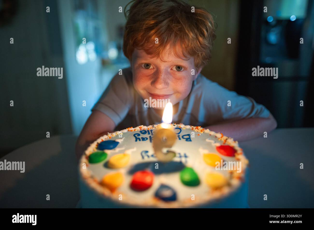 Garçon souriant célébrant l'anniversaire avec bougie incandescente sur gâteau coloré Banque D'Images