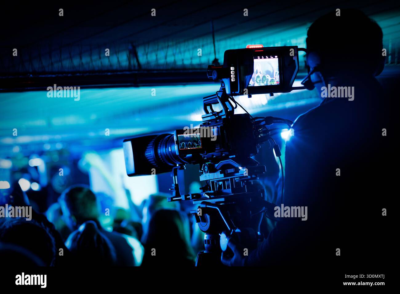 Vue rapprochée du cameraman exploitant la caméra vidéo professionnelle pendant le concert en direct dans un éclairage bleu. Banque D'Images