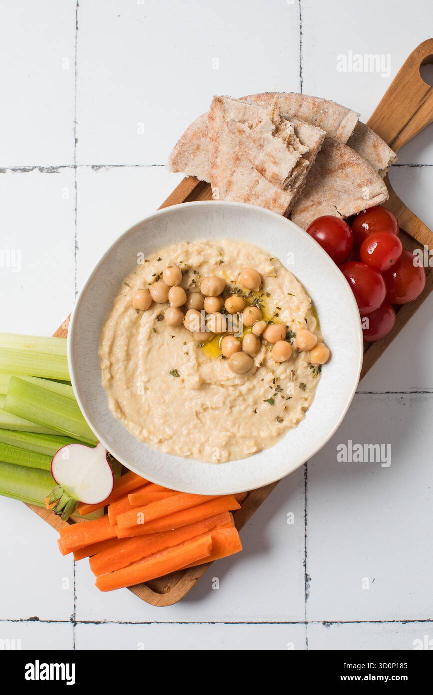 Houmous frais dans un bol sur une planche de bois avec pita, céleri et carottes. Plats de pois chiches, plat végétarien. Nourriture saine Banque D'Images
