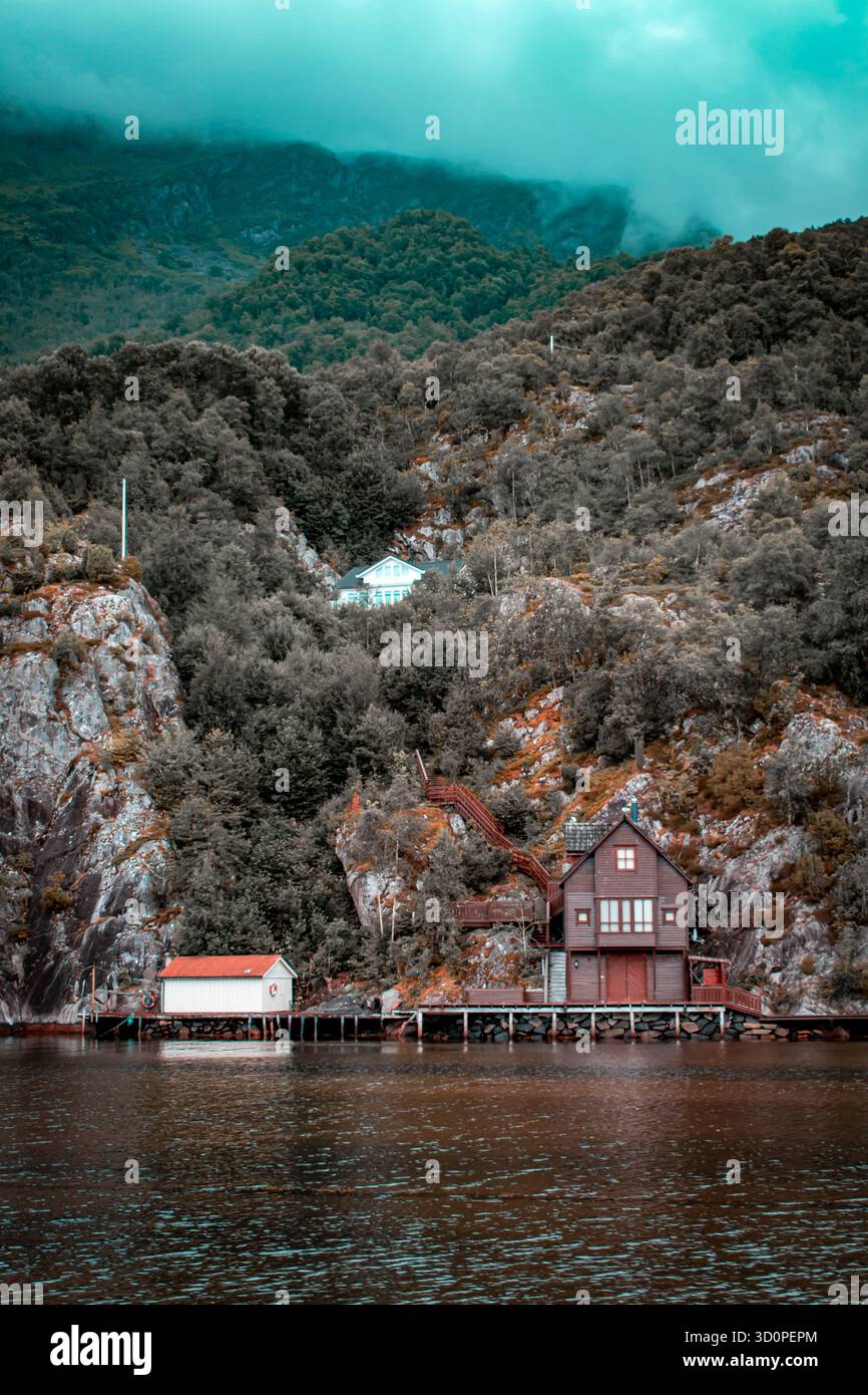Une cabane de pêche sur la rive, entourée de hautes falaises couvertes de forêt. Le brouillard s'est installé sur les sommets des montagnes. Banque D'Images