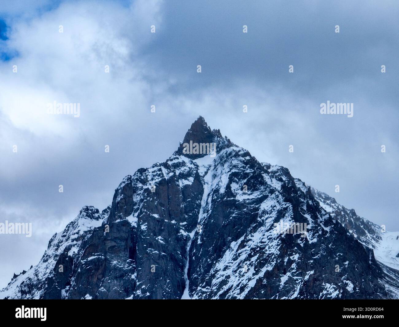 Vue aérienne rapprochée d'un sommet de montagne enneigé et isolé sous un ciel sombre, couvert et bleu foncé Banque D'Images