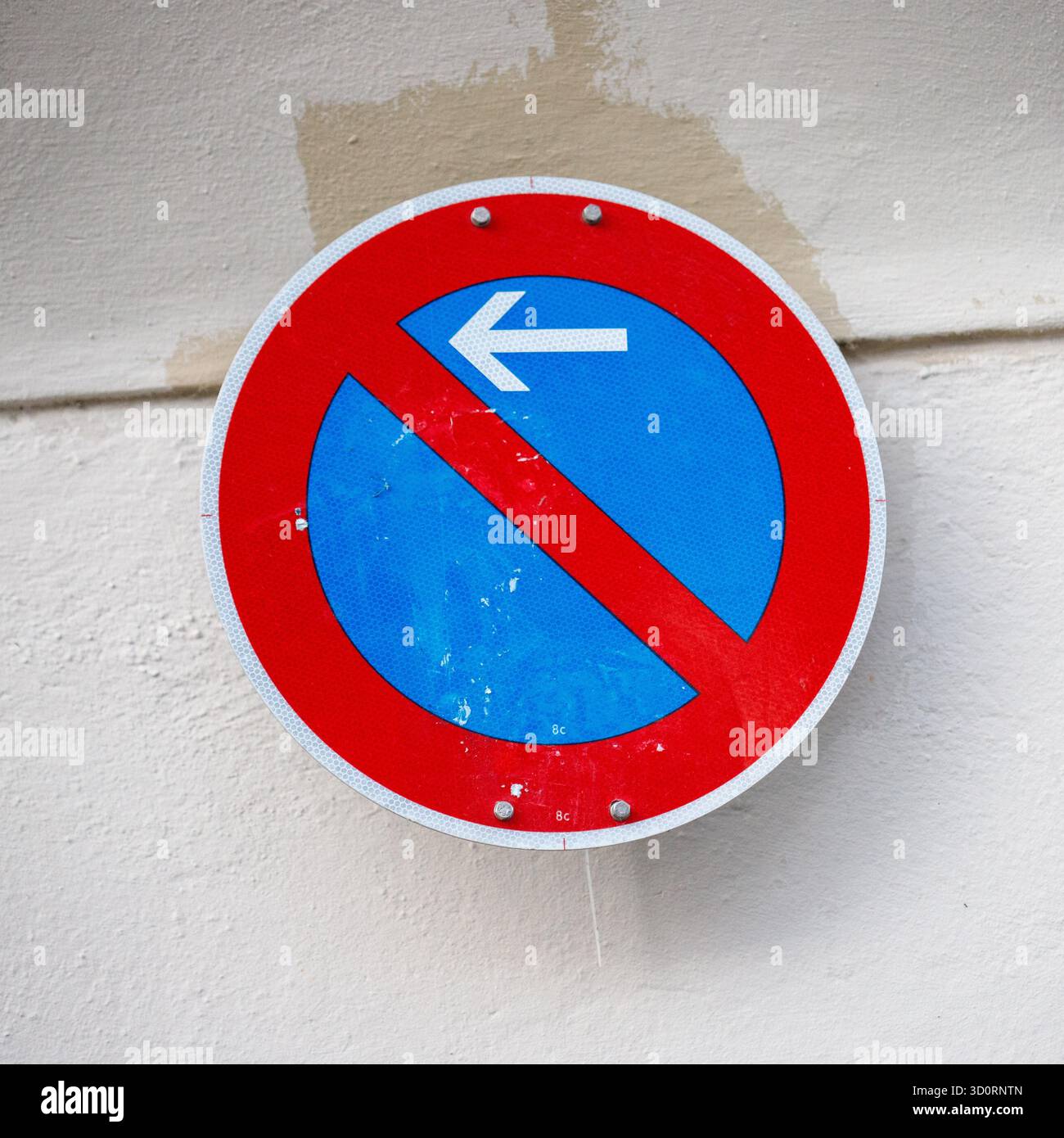 Un panneau de signalisation circulaire avec une bordure rouge, un centre bleu et une barre oblique rouge indiquant « pas de stationnement ». Une flèche blanche pointe vers la gauche. Banque D'Images