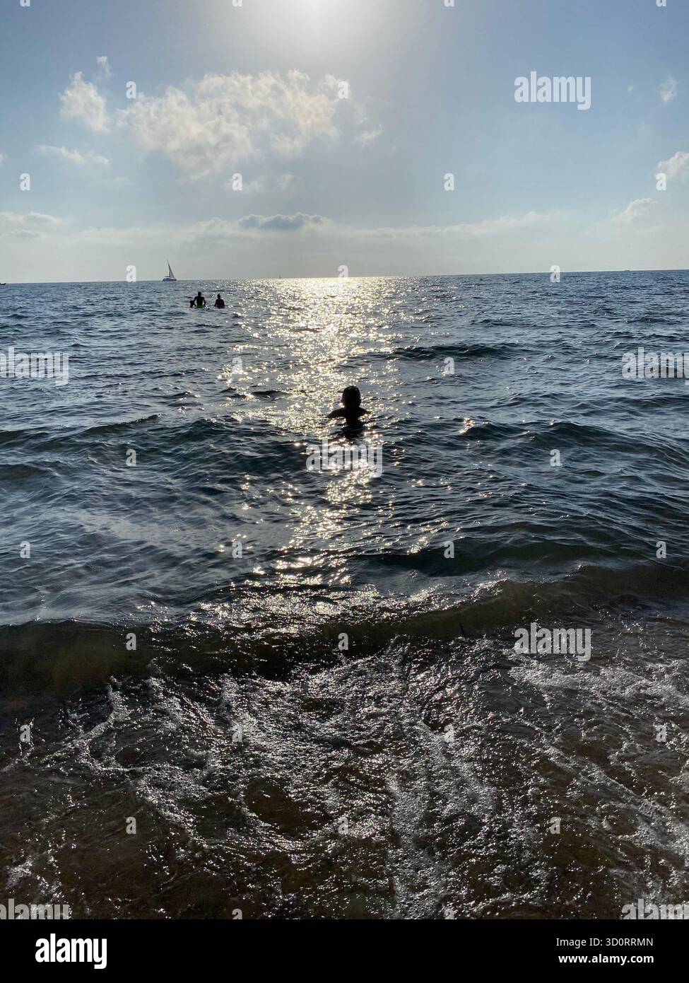 Vue sur la mer Méditerranée avec une eau sombre chatoyante et des silhouettes de personnes nageant dans la lumière calme. - Image de stock capturée avec un smartphone