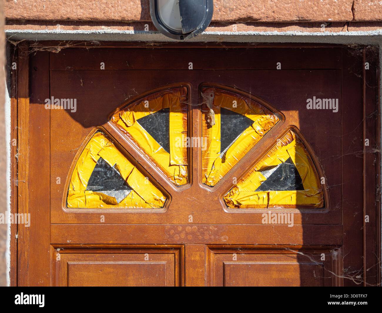 Porte en bois avec des vitres brisées recouvertes de ruban jaune. Banque D'Images