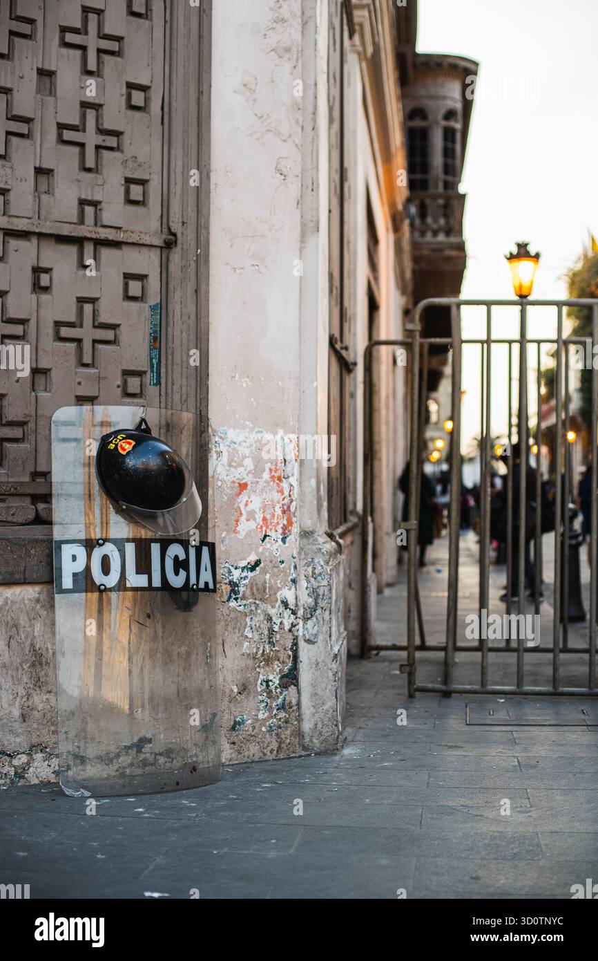 Bouclier antiémeute de la police et casque appuyés contre un vieux mur colonial dans le centre de Lima, Pérou, 2024. Scène urbaine reflétant la présence de la sécurité. Banque D'Images