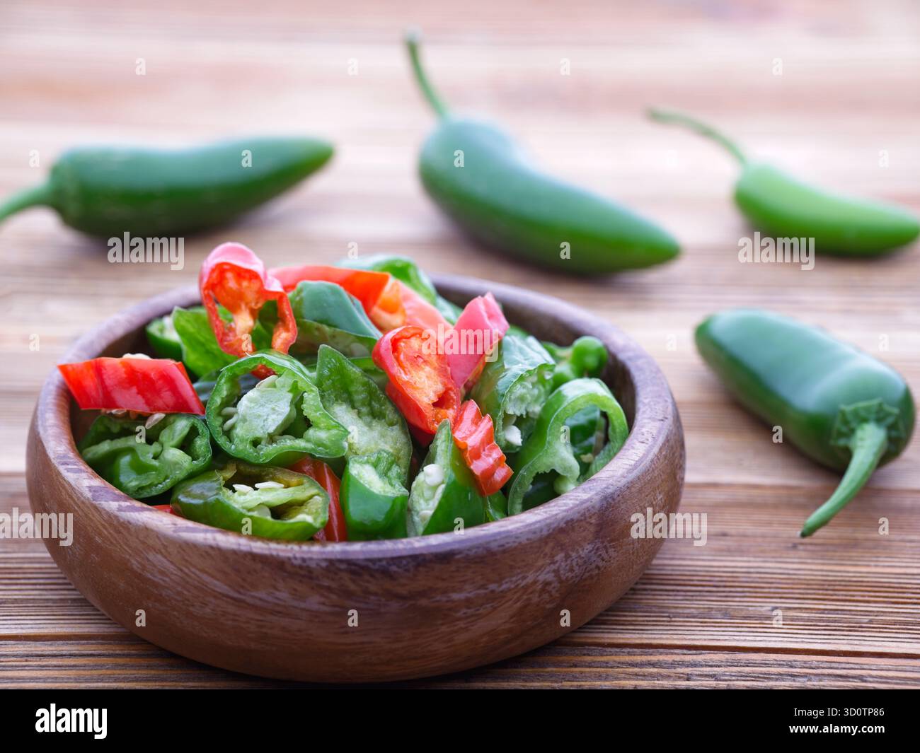 Une photo rapprochée d'un bol en bois rempli de poivrons verts et rouges tranchés. Banque D'Images