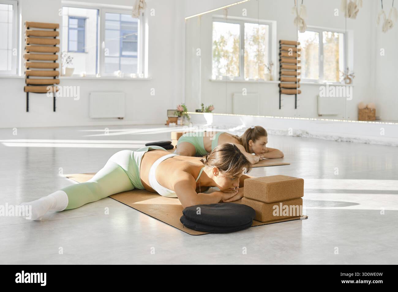 Dans un studio de yoga spacieux et bien éclairé, deux femmes sont engagées dans une routine d’étirement sur tapis. Ils se concentrent sur leur pratique, entourés de paisible de Banque D'Images