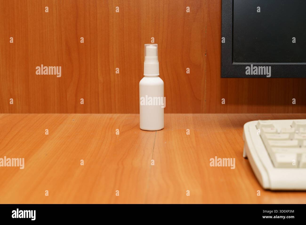Un vaporisateur blanc propre se trouve sur un bureau en bois à côté d'un écran d'ordinateur et d'un clavier dans un espace de travail bien rangé. Banque D'Images