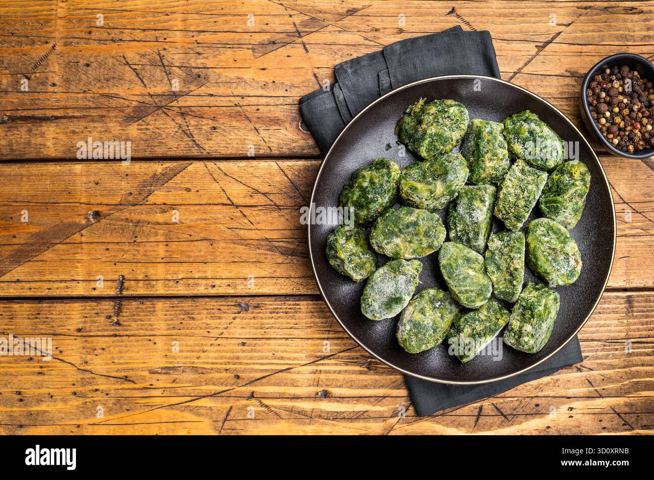 Blocs d'épinards surgelés crus et nutritifs sur une assiette sombre, prêts à être décongelés et cuits. Photographie culinaire rustique traditionnelle Banque D'Images