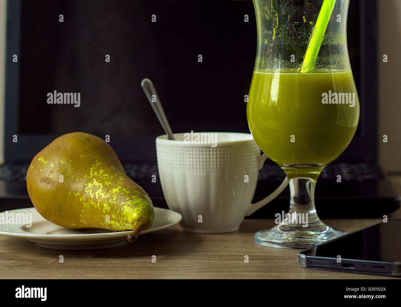Jus vert ou cocktail ou smoothie, poire de conférence vert mûr et une tasse de café blanche près de l'ordinateur portable sur le bureau Banque D'Images