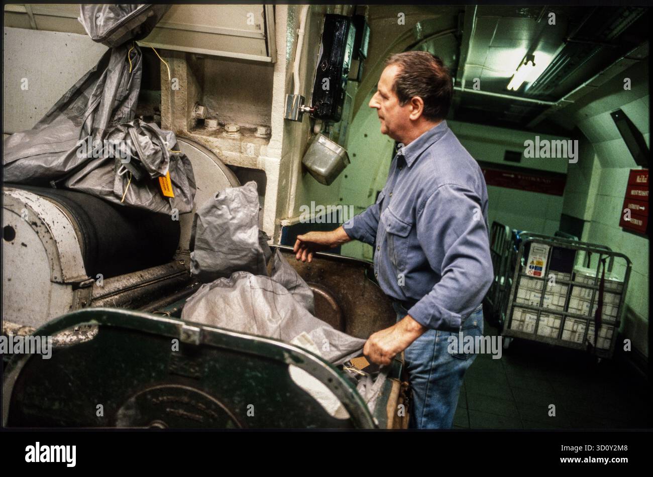 Ouvrier postal chargeant des sacs postaux sur une bande transporteuse. Train postal souterrain Mount Pleasant, Londres, Royaume-Uni. 1990s. Banque D'Images