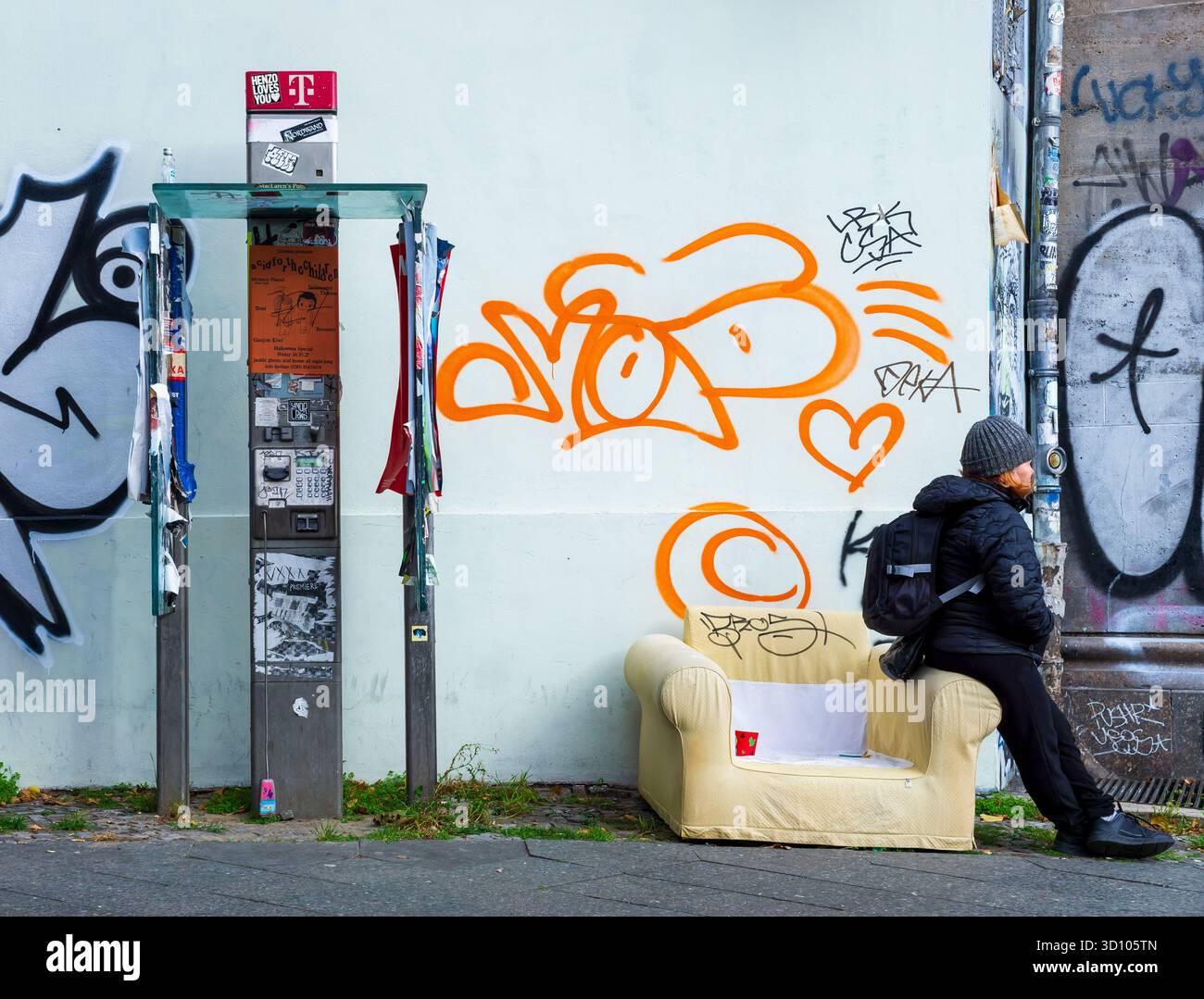 Vieux téléphone telekom public à côté d'une femme assise à Berlin, en Allemagne, symbolisant la solitude, l'isolement. Photographie de rue authentique. Banque D'Images
