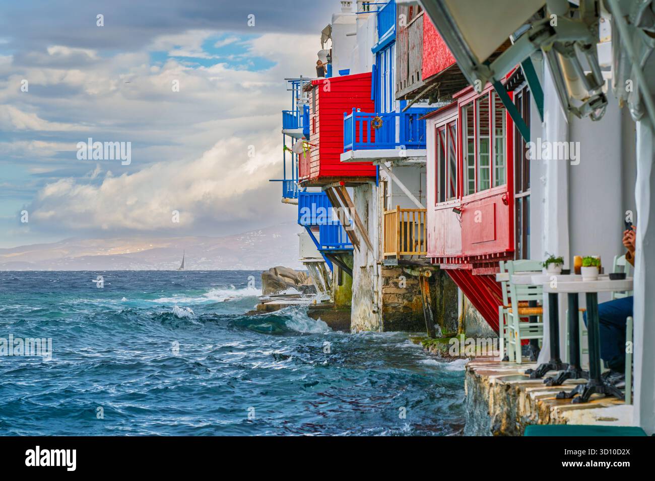 Des bâtiments colorés avec balcons surplombent la mer Égée à côté de cafés en plein air alors que les vagues frappent la côte dans le quartier de Little Venice à Mykonos, en Grèce. Banque D'Images