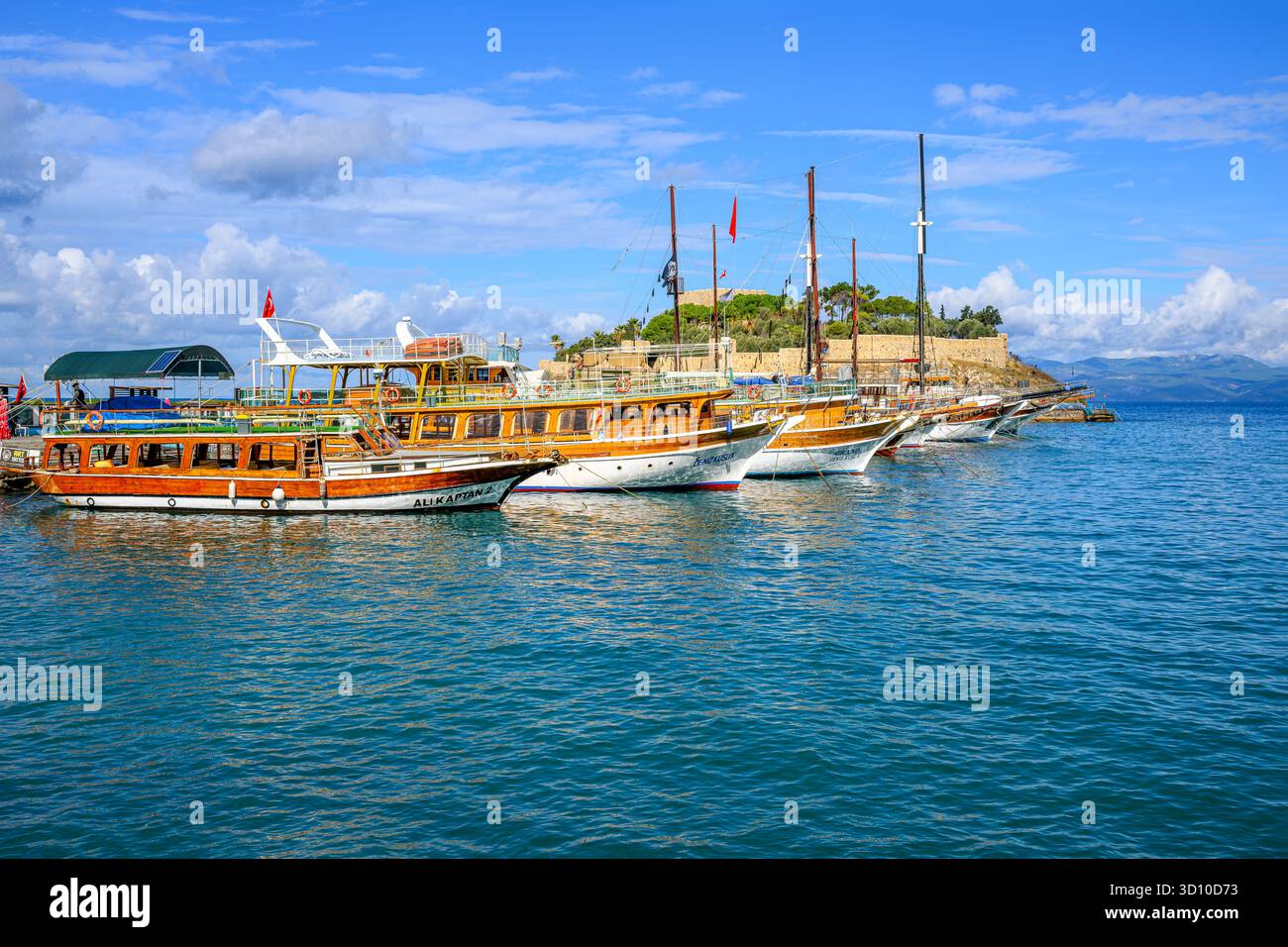 Des bateaux d'excursion colorés et historiques bordent la jetée sur l'île aux pigeons avec le château de Kusadasi derrière, à Kusadasi, en Turquie. Banque D'Images