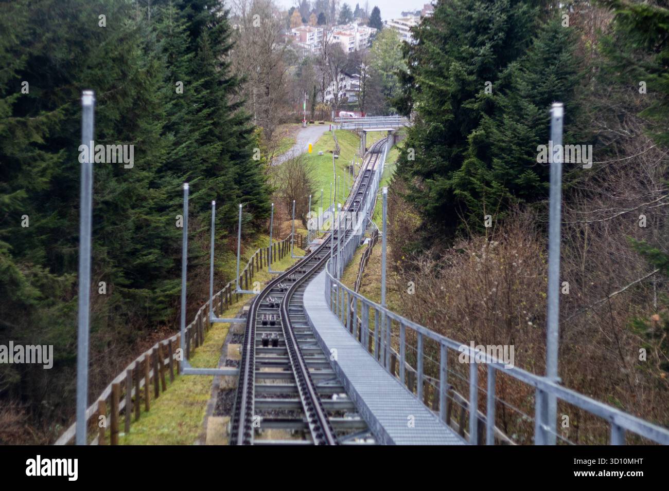 Funiculaire voie ferrée ascendante sur une pente raide, entourée d'arbres verts avec des bâtiments visibles au loin Banque D'Images