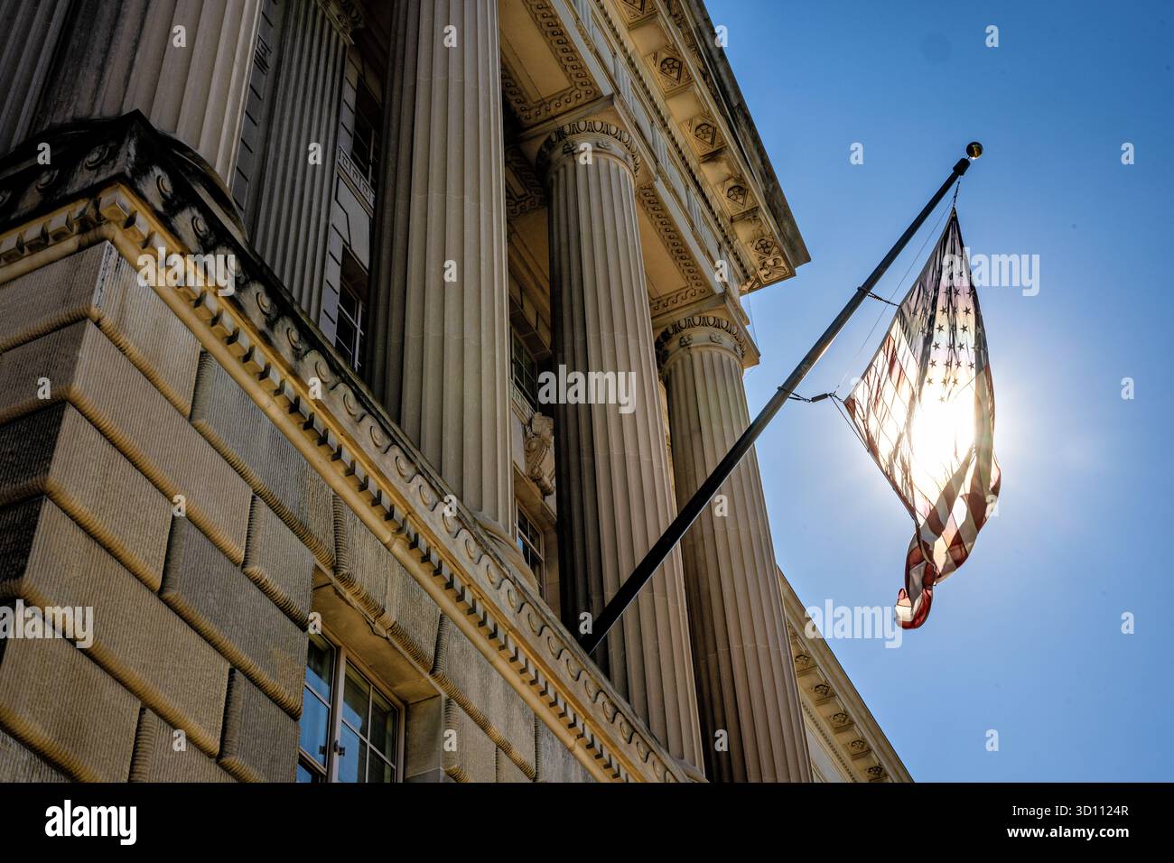 DRAPEAU AMÉRICAIN rétroéclairé par le soleil sur le Herbert C. Hoover Federal Building Washington DC // WASHINGTON DC — Un drapeau américain est rétroéclairé par le soleil sur le Herbert C. Hoover Building, le siège du Département du commerce des États-Unis. Achevée en 1932, cette importante structure néoclassique porte le nom du 31e président des États-Unis, Herbert C. Hoover. C'est un élément clé du complexe du Triangle fédéral, abritant divers organismes gouvernementaux dans la capitale nationale. Banque D'Images