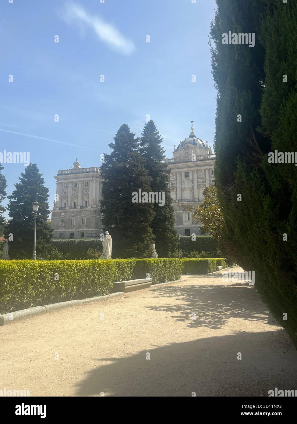 Palais royal de Madrid vu à travers les arbres dans Jardines de Sabatini avec statues, Pathway et ciel bleu lumineux lors d'une journée d'été ensoleillée. - Image de stock capturée avec un smartphone