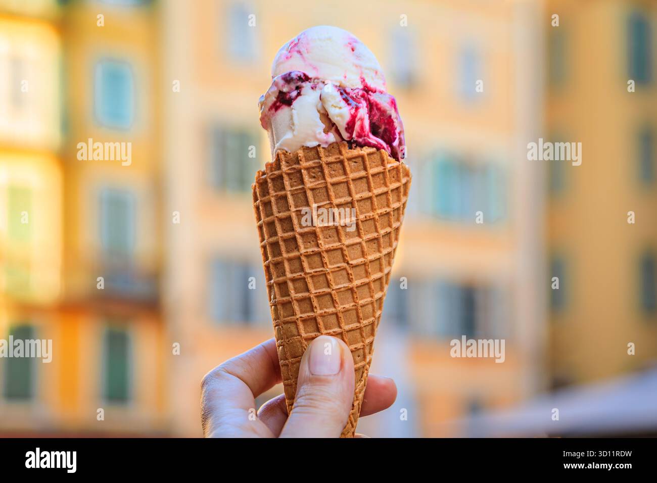 Main tient un cône de chocolat artisanal et amarena cerise gelato, vue sur les maisons colorées traditionnelles, vieille ville vieille ville, Nice, Sud de la France Banque D'Images
