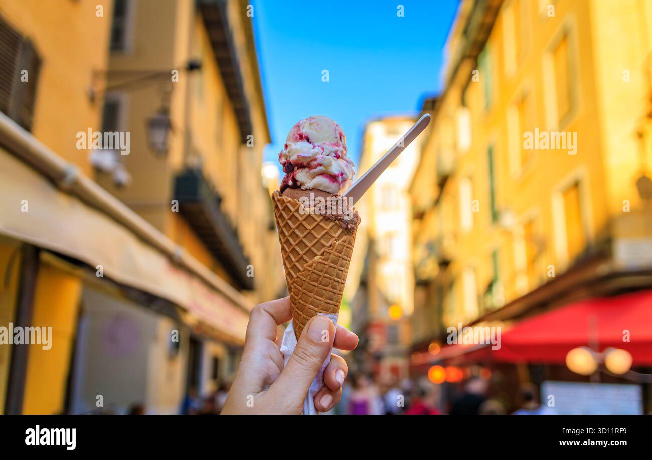 Main tient un cône de chocolat artisanal et amarena cerise gelato, vue sur les maisons colorées traditionnelles, vieille ville vieille ville, Nice, Sud de la France Banque D'Images