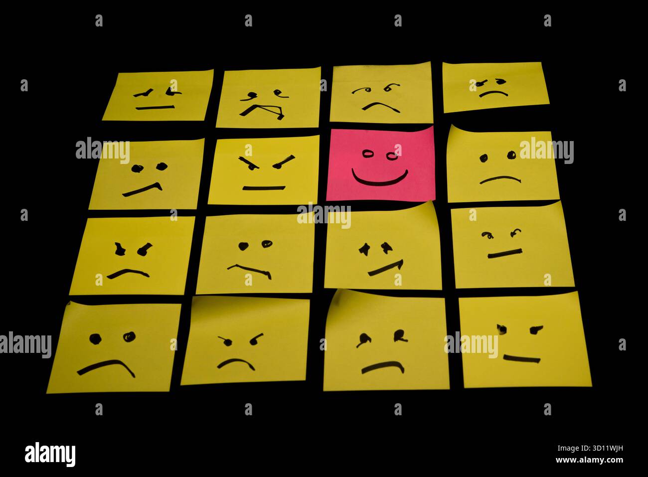 15 papiers jaunes placés parallèlement les uns aux autres avec des visages dessinés sur eux exprimant la colère ou la tristesse, face à un papier rose avec un visage exprimant le happin Banque D'Images