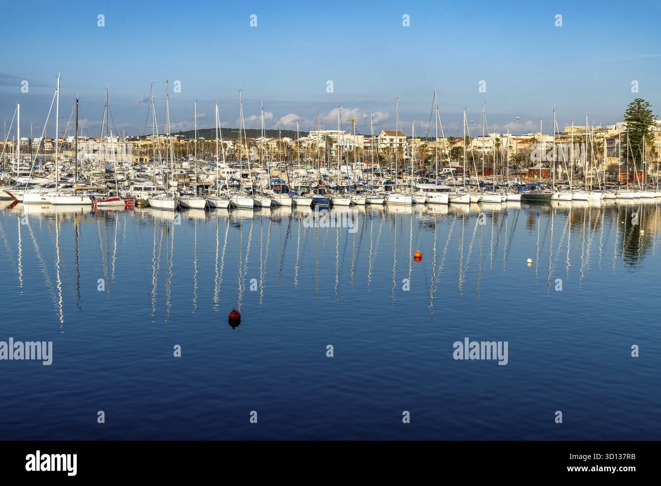 Alghero, Sardaigne - Italie - 2025 : les voiliers sont amarrés au quai avec de hauts mâts reflétant dans l'eau calme. Le ciel lumineux, les bouées rouges et le mode Banque D'Images