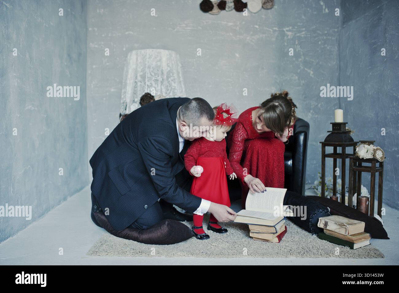 Famille heureuse avec sa fille lire le livre ancien sur fond tapis décor vintage prix avec Banque D'Images
