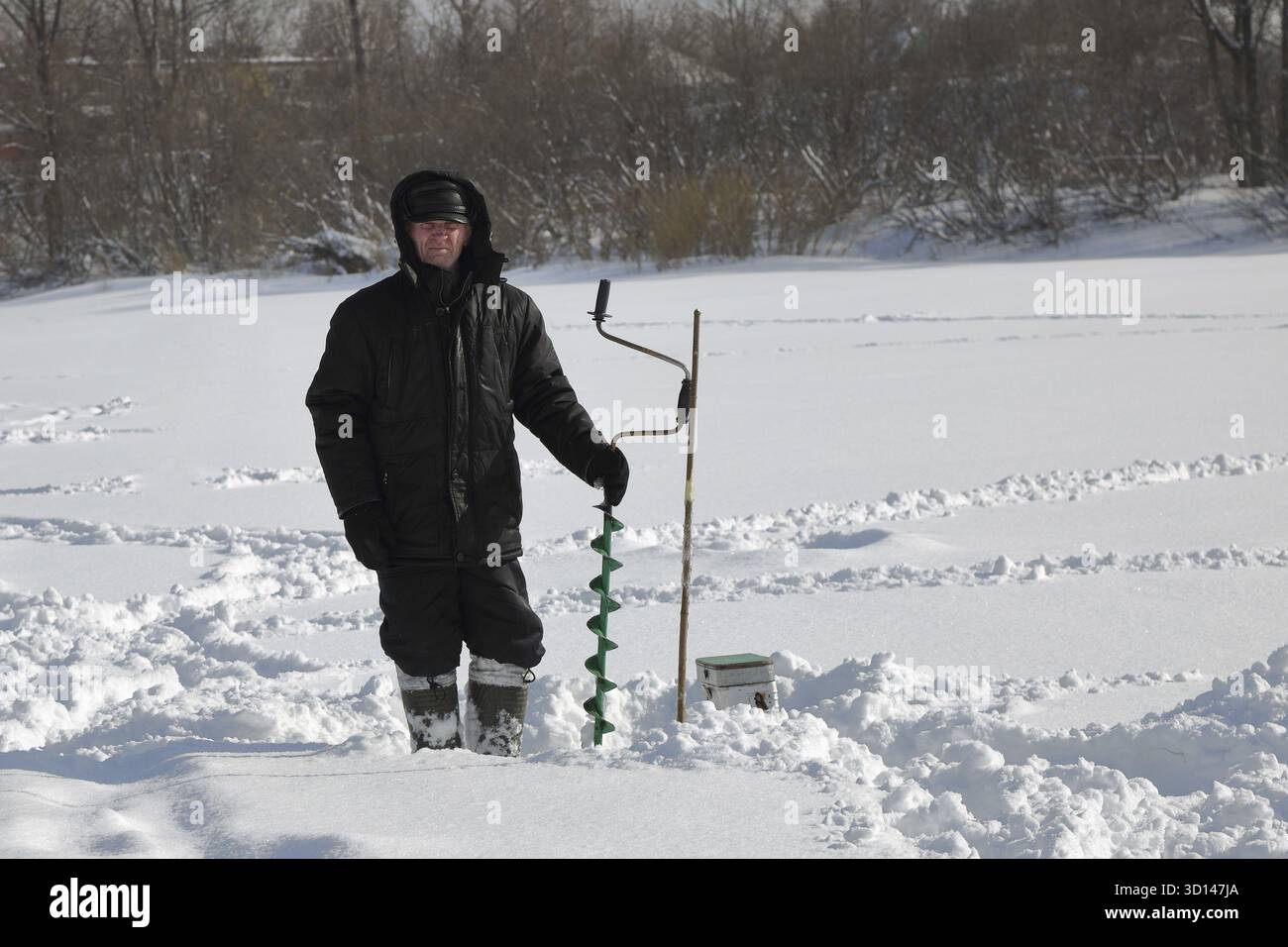 Pêcheur d'hiver avec des vis de glace sur la glace de rivière Banque D'Images