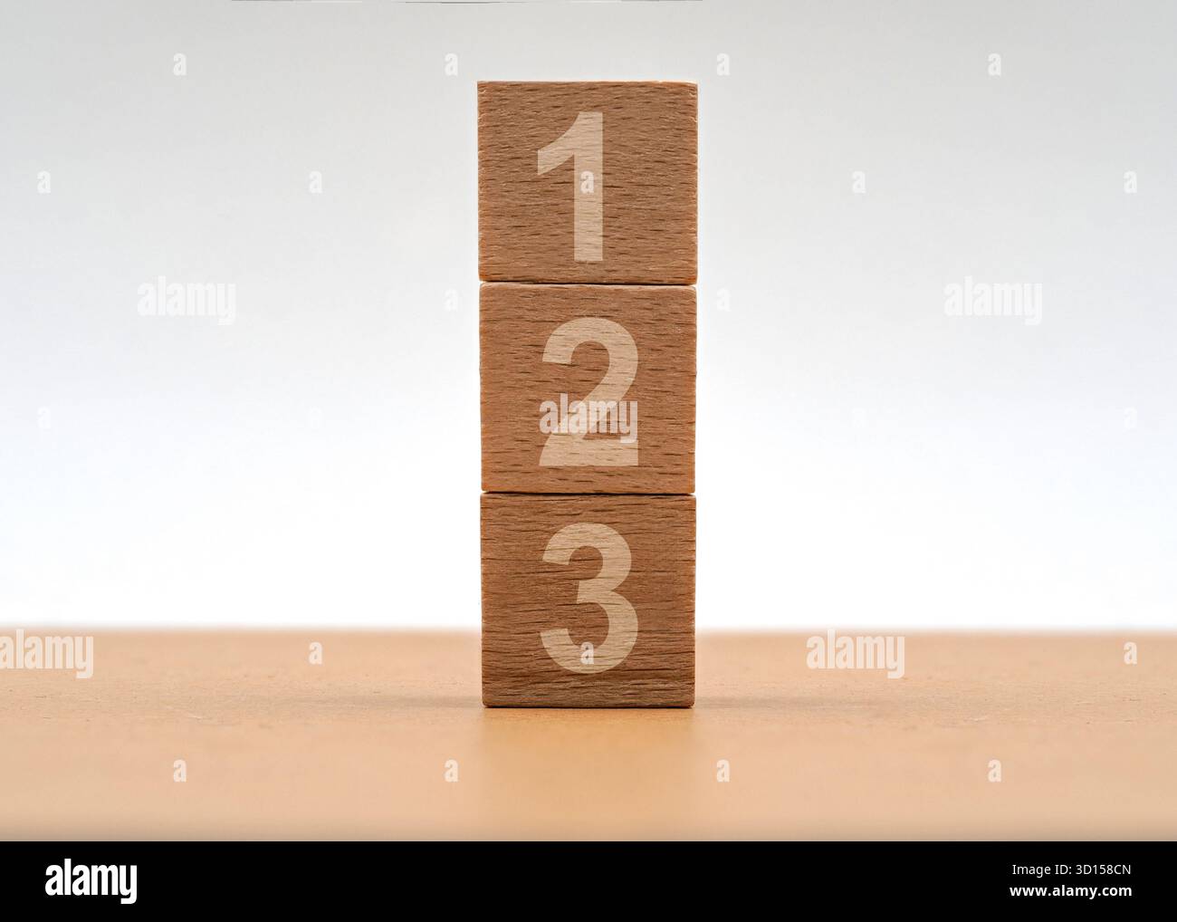 Trois blocs de bois sont empilés les uns sur les autres, chacun affichant un nombre de un à trois. Le réglage est simple et met en évidence le nat des blocs Banque D'Images