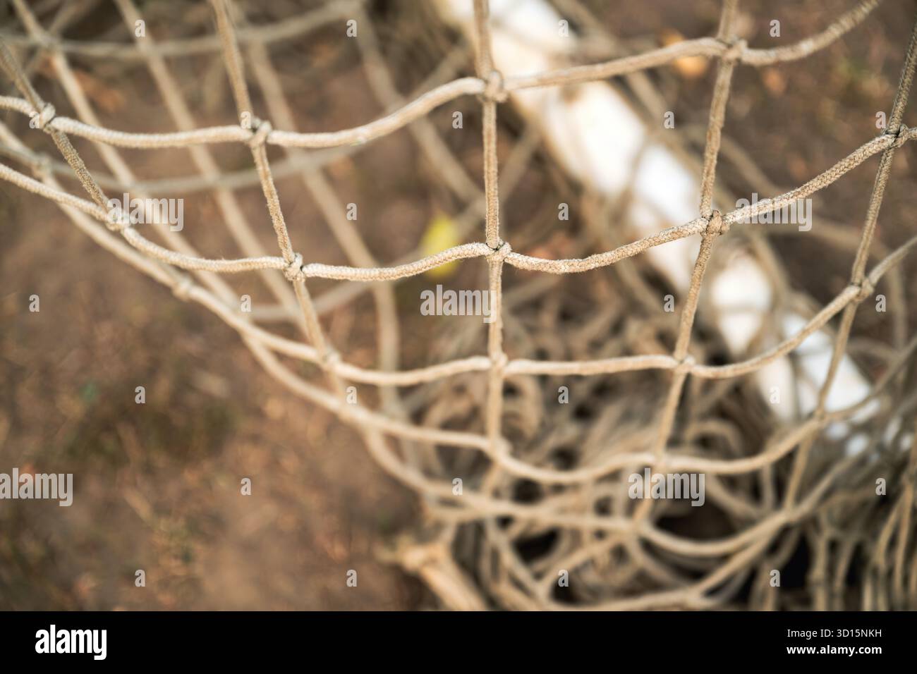 Gros plan d'un vieux filet de but de football usé montrant des fibres effilochées et une texture altérée. Mise au point sélective. Banque D'Images