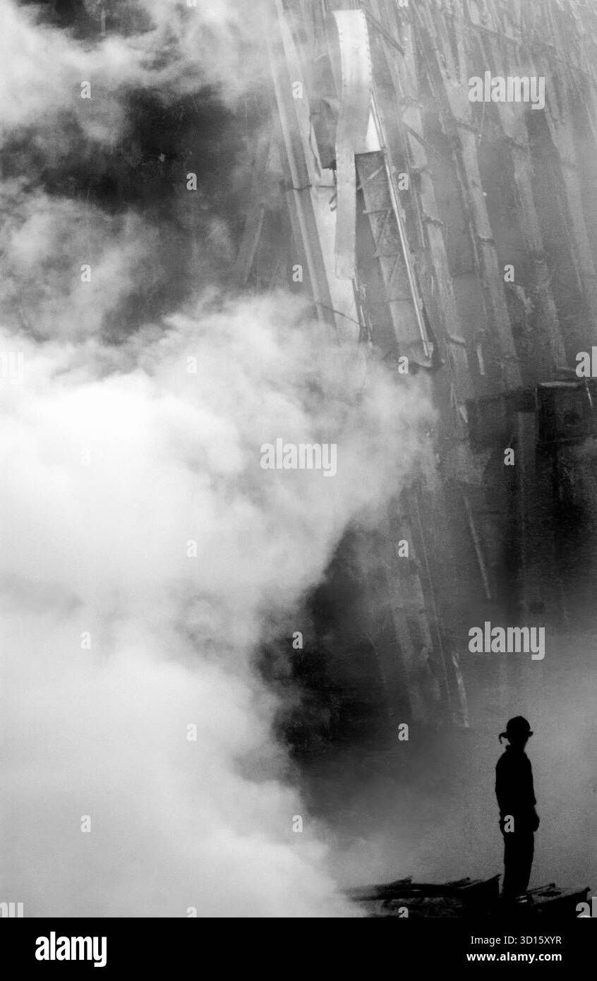 Un pompier est solitaire regardant comme la fumée monte dans les décombres et les débris du World Trade Center à New York City dans le domaine savent comme Ground Zero, après les attaques terroristes du 11 septembre. Banque D'Images Un pompier est solitaire regardant comme la fumée monte dans les décombres et les débris du World Trade Center à New York City dans le domaine savent comme Ground Zero, après les attaques terroristes du 11 septembre. Banque D'Images