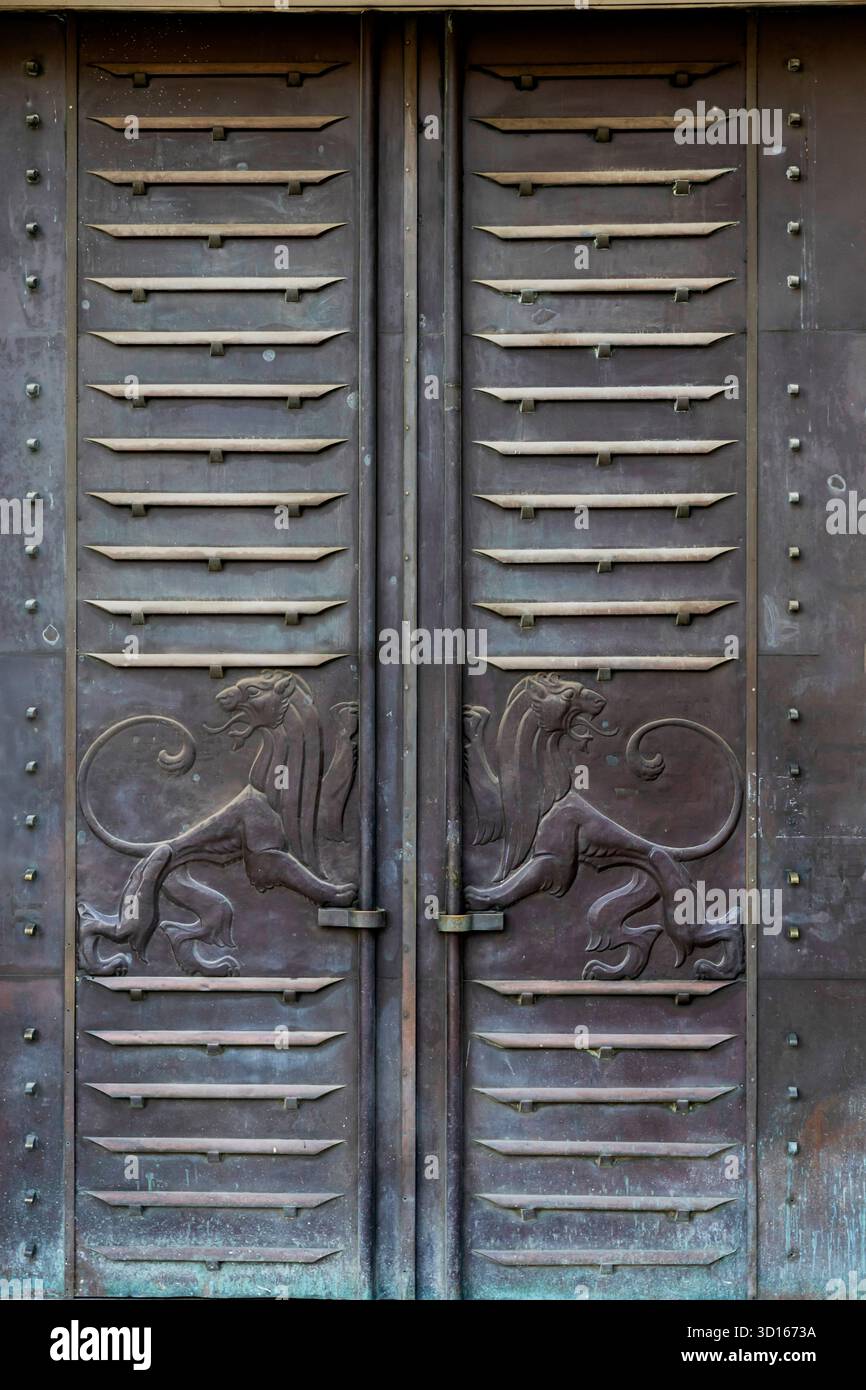 Gros plan d'une grande porte en métal vieilli avec des lattes horizontales surélevées et deux figurines de lion sculptées tournées vers l'extérieur, représentant le symbole O. Banque D'Images
