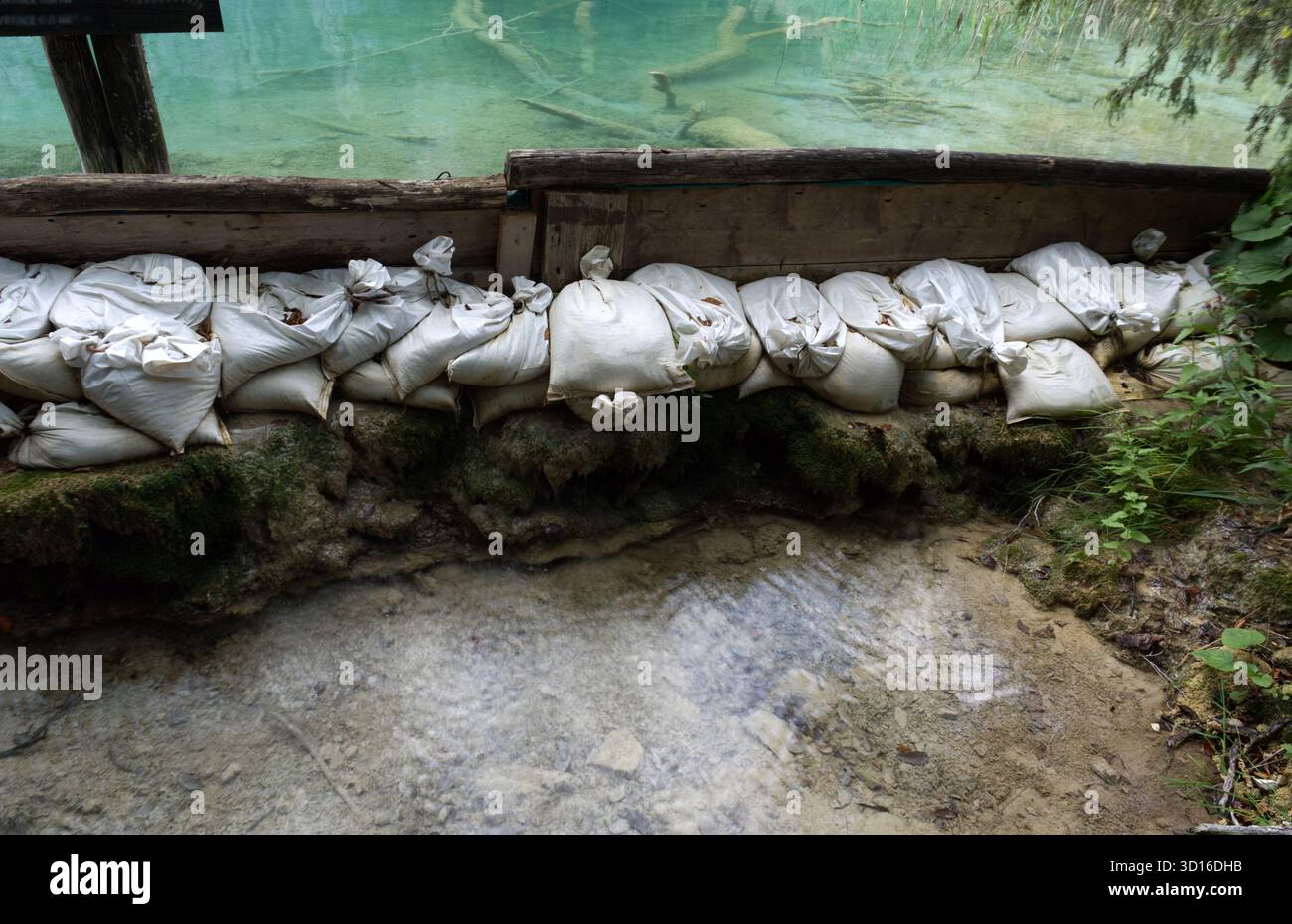 Des sacs de sable blancs bordent une rive humide, formant une barrière protectrice contre la montée de l'eau. Banque D'Images