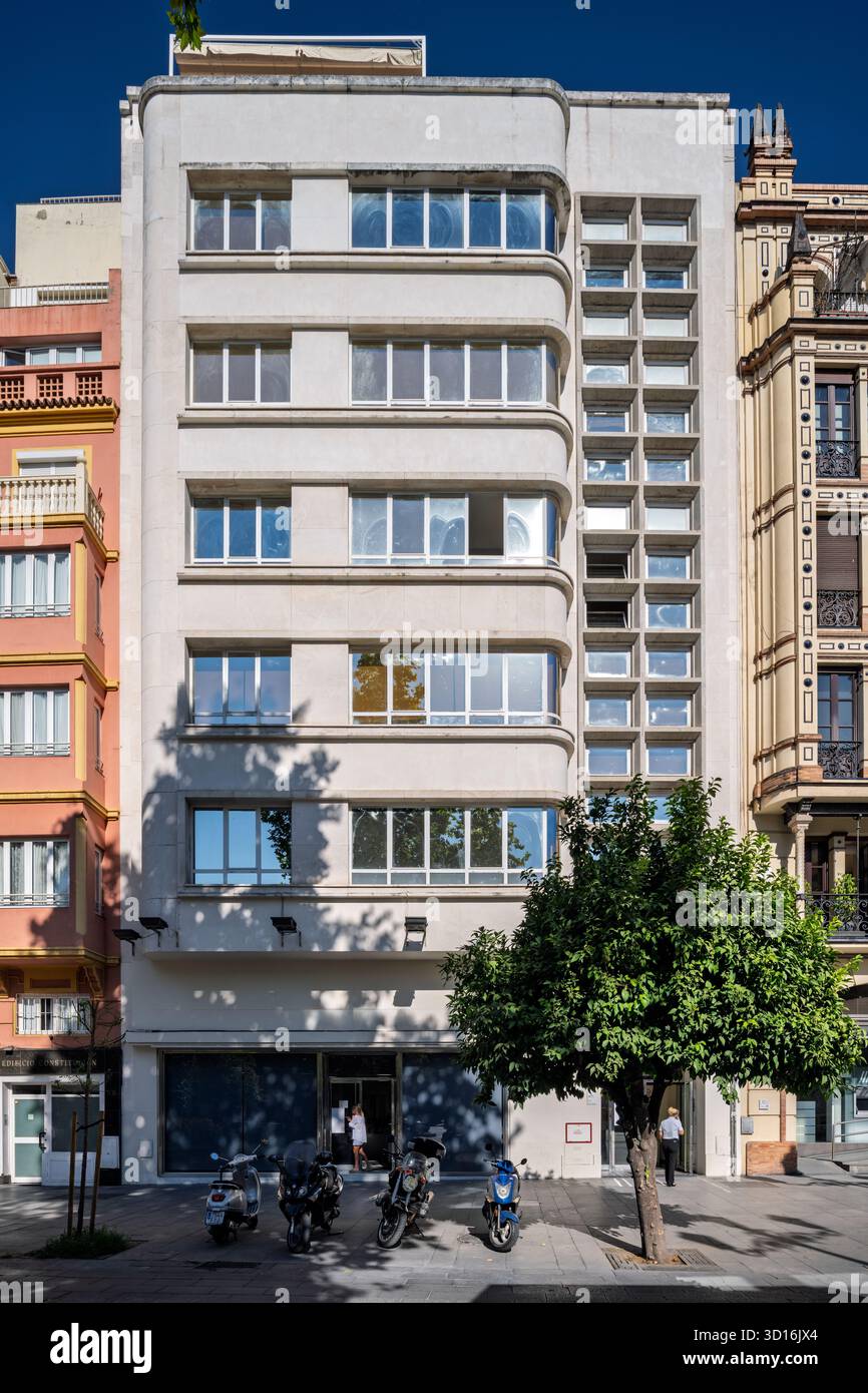 Ce bâtiment rationaliste de 1936 à Séville met en valeur le design moderniste parmi les structures historiques, avec un arbre et des motos stationnées. Banque D'Images